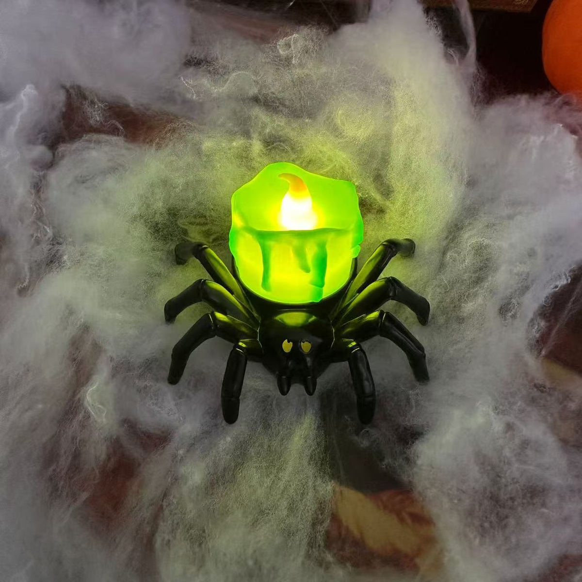 Black spider decoration holding a glowing green candle-style light.