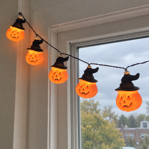 Pumpkin witch-hat string lights by a cozy window — AI-generated lifestyle scene.